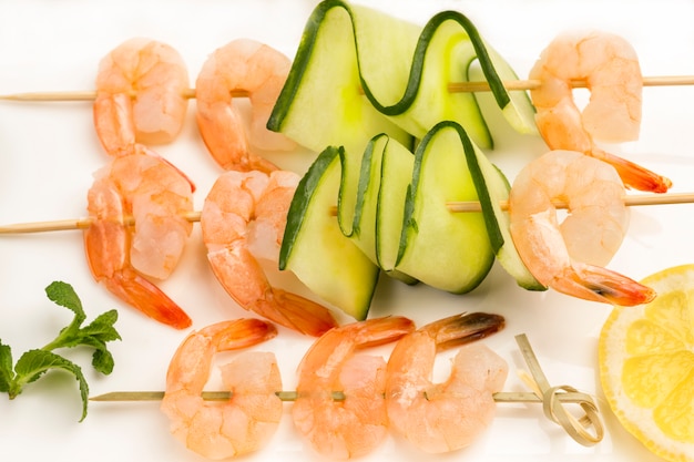 Shrimps with cucumber and tomatoes on skewer in white plate