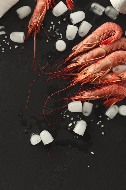 Shrimps with ice cubes and sea salt on black background, copy\
space. top view on appetizing seafood snack, restaurant serving\
backdrop.