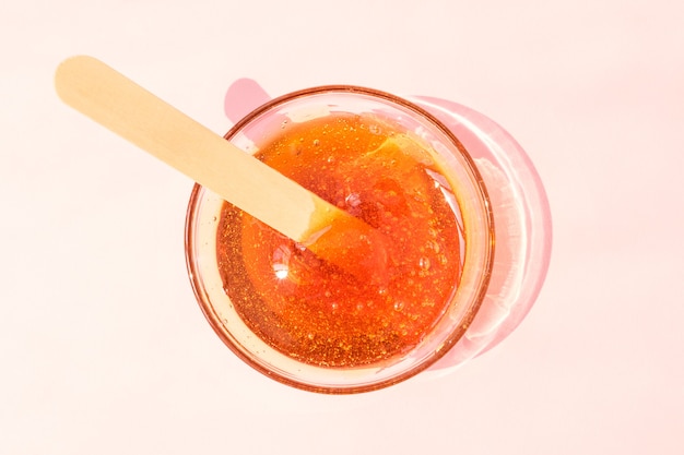 Shugaring paste in a glass bowl on a pink background. Hair removal, epilation, wooden spatula for sugaring paste