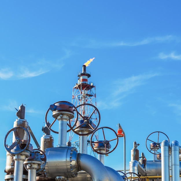 Photo shutoff valves of a gas processing plant against the background of a blue sky and a flare pipe