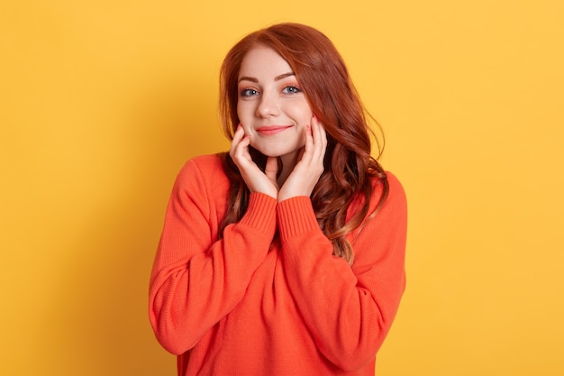 Shy delightful pleased female keeps hands on cheeks