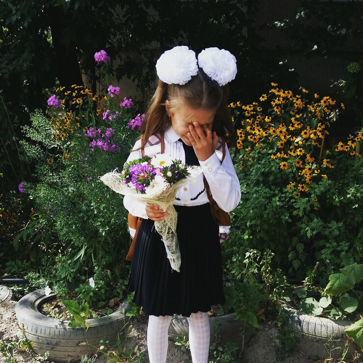 Photo shy girl holding bouquet while standing against flowering plants