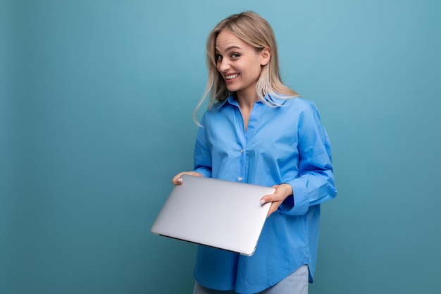 Shy laughing blond girl student with a laptop computer on a bright blue background