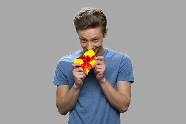 Foto ragazzo teenager timido che tiene piccolo contenitore di regalo. bel ragazzo adolescente con la presente casella in piedi su sfondo grigio.