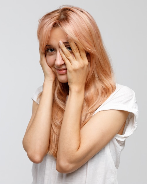 shy timid woman with long blonde hair covering her face with hand, smiling and peeking through fingers
