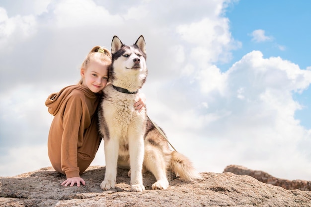 Siberian husky and his beautiful blueeyed mistress are sitting on a rock against the sky The concept of love for animals and nature