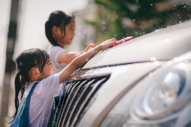 姉妹のアジアの女の子が車を洗い、夏の暑い日に屋内で楽しく遊んでいます