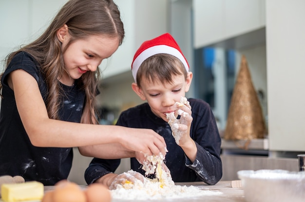 兄弟は、クリスマスの帽子をかぶった男の子で、台所で料理をして浮気しています。幸せな子供のアイデア