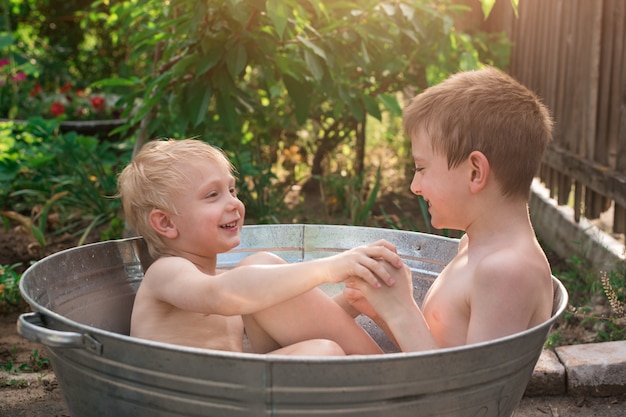 Siblings bathe in basin outdoors and play splash. Holiday village