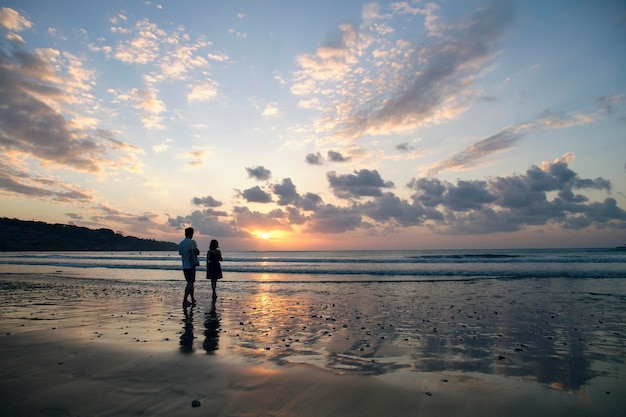 siblings at beach against sky during sunset