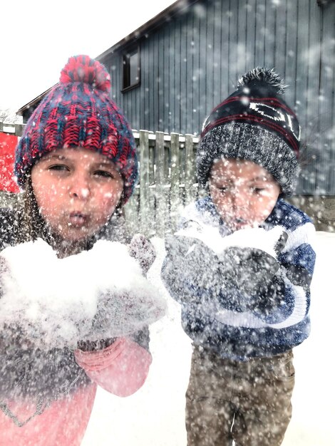 Foto fratelli che soffiano la neve durante la nevicata