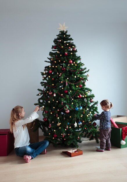 Siblings decorating christmas tree against wall at home