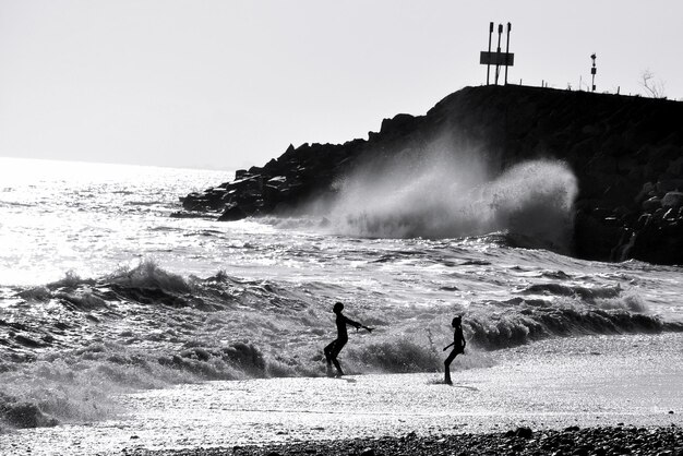 Siblings enjoying on shore at beach against sky