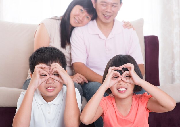 사진 부모 가 배경 에 앉아 있는 동안 손가락 으로 안경 을 만드는 형제자매 들