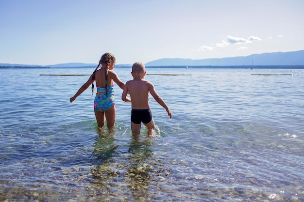 Братья и сестры идут в воду под солнечным светом, веселятся, радуются летним каникулам и путешествуют по женевскому озеру