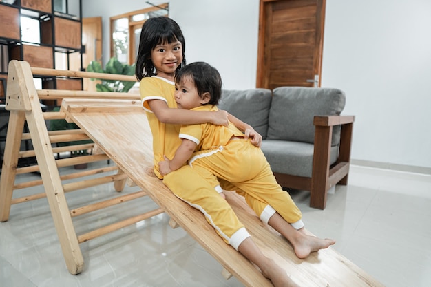 The siblings hug while playing slide in the Pikler Triangle Toy together in the living room