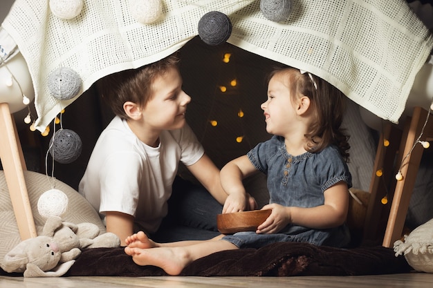 Siblings in a hut of chairs and blankets. Brother and sister playing at home