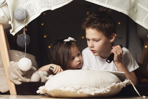 Siblings lie in hut of chairs and blankets