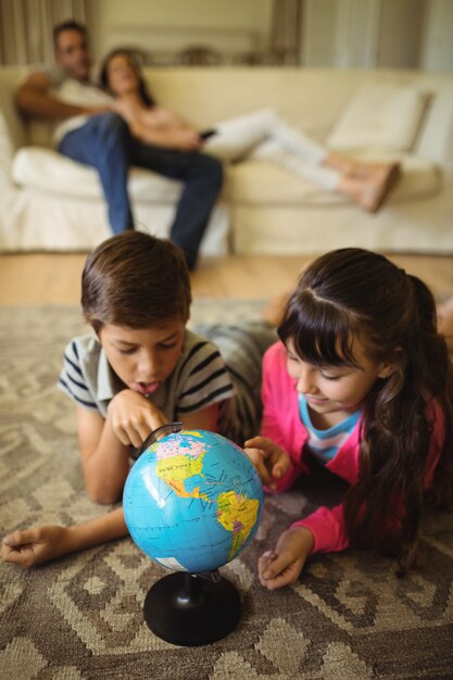 Siblings lying and looking at globe in living room