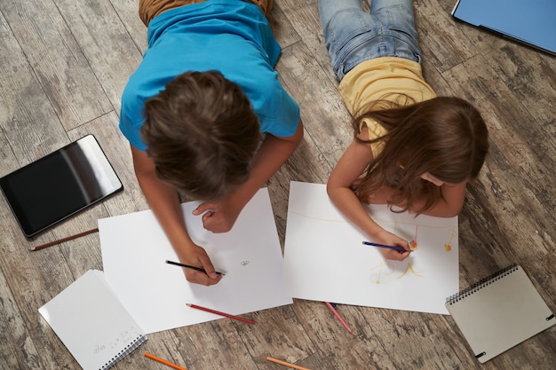 Siblings playing together at home top view of little boy and girl lying on the wooden floor and