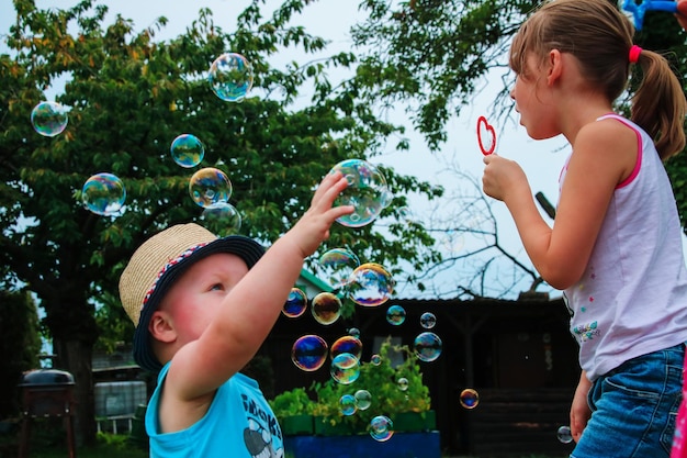 Photo siblings playing with bubbles against trees