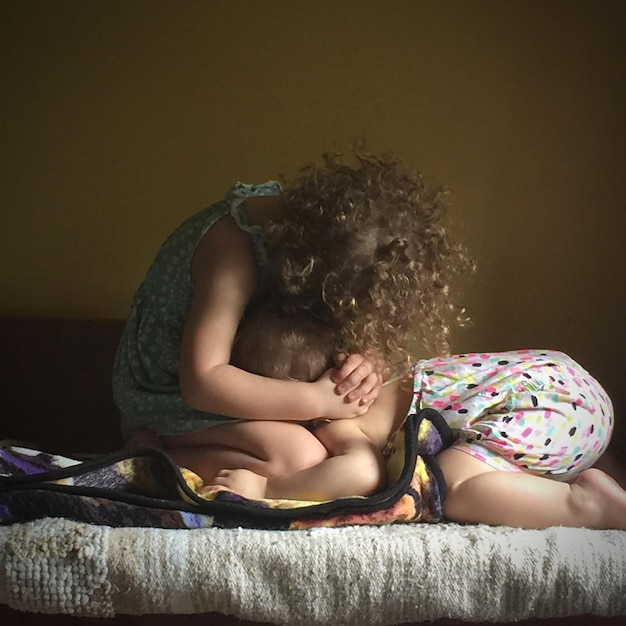 Photo siblings sitting on bed at home