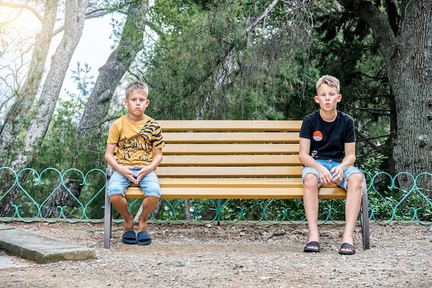 Siblings sitting on wooden bench look with upset and disappointed expressions