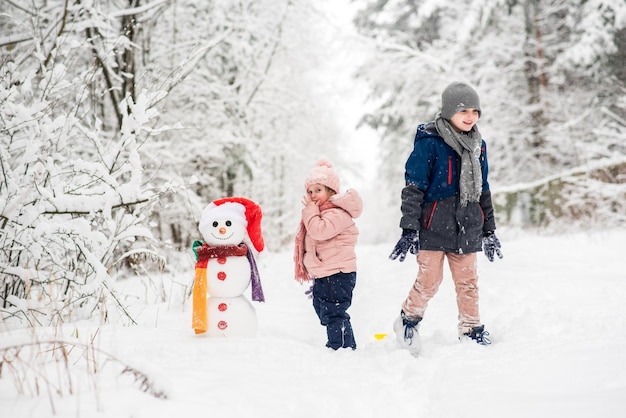 Photo siblings standing with snowman on snowy land