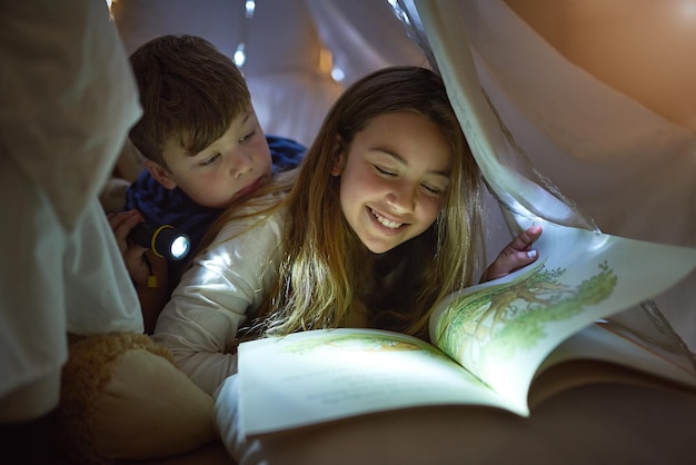 Siblings who enjoy story time together Cropped shot of siblings reading a story under a blanket fort at home