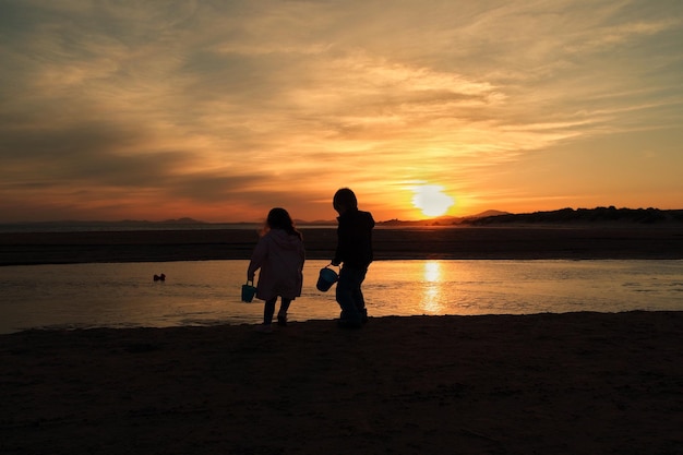 夕暮れの空に照らされたビーチで岸にバケツを持った兄弟姉妹