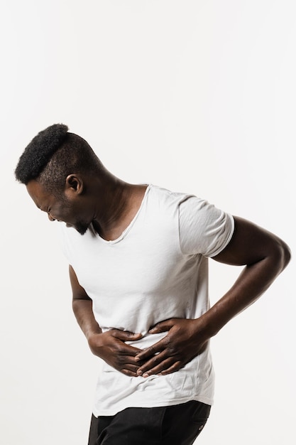 Больной афроамериканец держит живот, потому что он болит Панкреатит, заболевание поджелудочной железы воспаляется Рак желудка и пищевода африканца