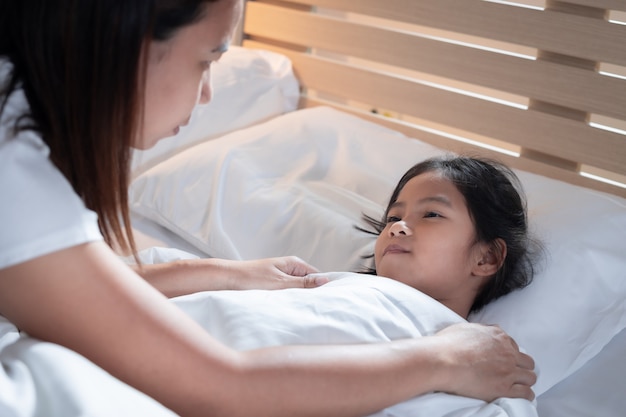 Sick asian child girl get sick and sleep on the bed, mother taking care and cover the blanket on her daughter