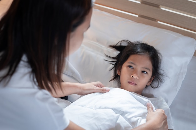 Sick asian child girl get sick and sleep on the bed, mother taking care and cover the blanket on her daughter