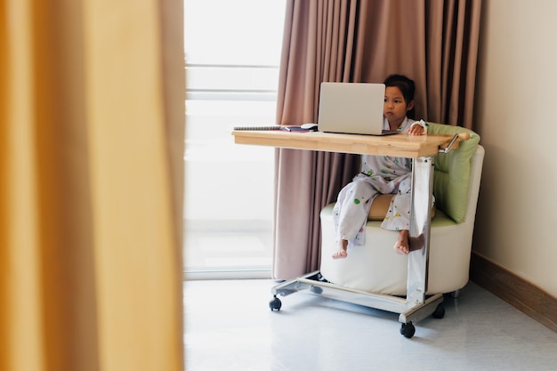 Sick asian child sitting and learning online class with teacher and friend while stay in private patient rooms in the hospital. Isolation homeschooling and distance learning.