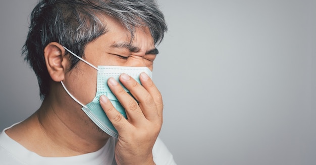sick asian man wearing a medical face mask and coughing and covering his mouth with my hand. concept of protection pandemic coronavirus and respiratory disease