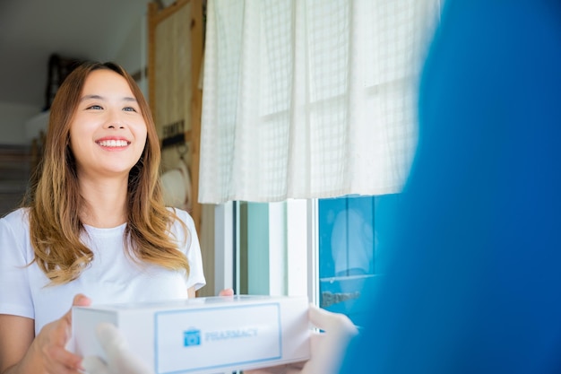 Sick Asian woman hand hold for receive medication first aid pharmacy box from hospital delivery service at front home, merchandise medicine, Delivery man give medicine drug store to patient female