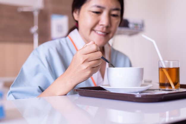 Больная азиатка пациентка ест еду на больничной койке в больнице