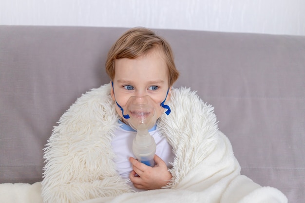 Sick baby boy with inhaler treats throat at home the concept of health and inhalation treatment