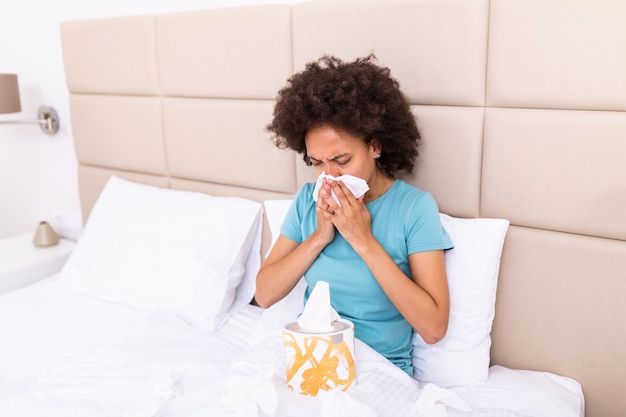 病気の黒人の女の子がベッドの上に座る不健康な吹くランニング鼻