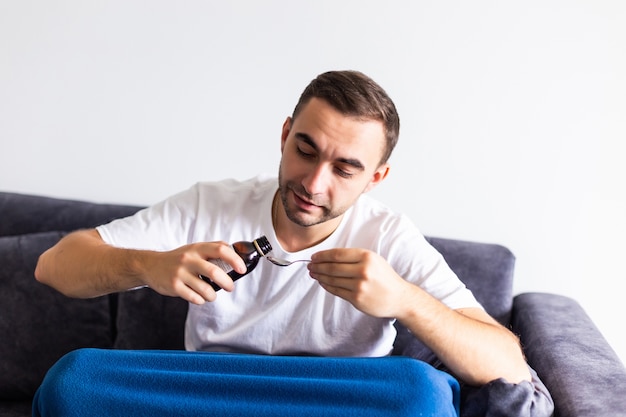 Sick black man dropping aspirin pill into glass of water sitting on couch at home free space