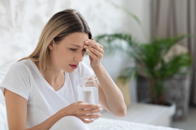 Sick blonde lady feeling bad touching head bedroom interior