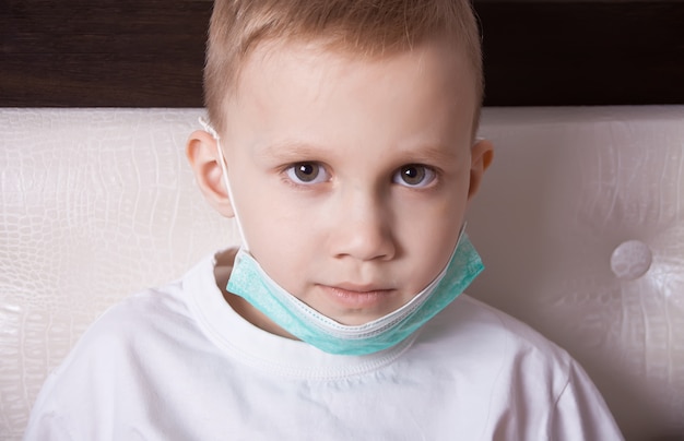 Sick boy sitting in bed in medical mask and doesn t feel well