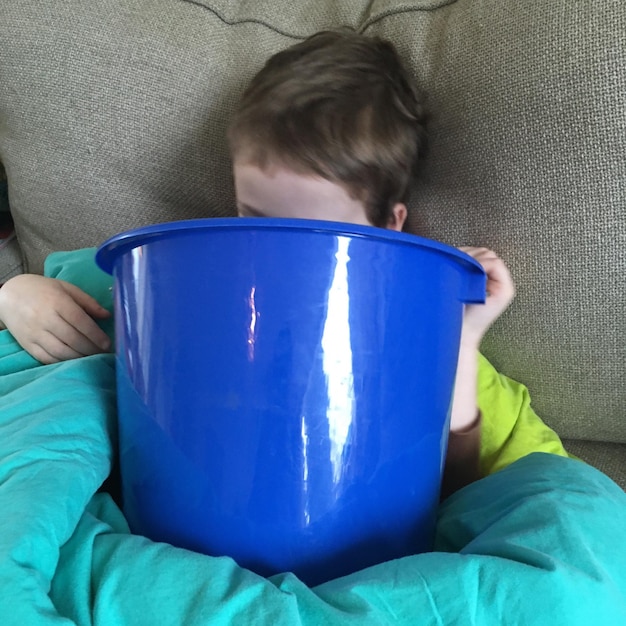 Sick boy vomiting in bucket while lying on bed