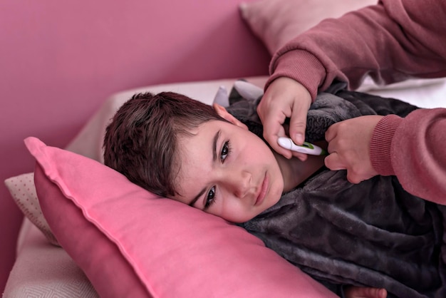 Sick boy with thermometer laying in bed and mother hand taking temperature mother checking temperatu