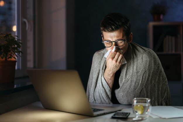 Sick businessman blowing nose while working on computer in home office