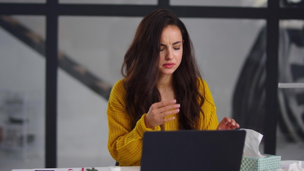 Sick businesswoman getting flu in office Ill woman sneezing near laptop indoor