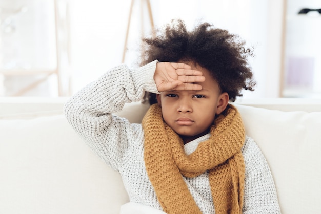 Photo sick child with flu sitting on couch at home.