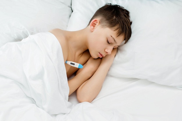 Больной ребенок с высокой температурой лежит в постели и держит термометр