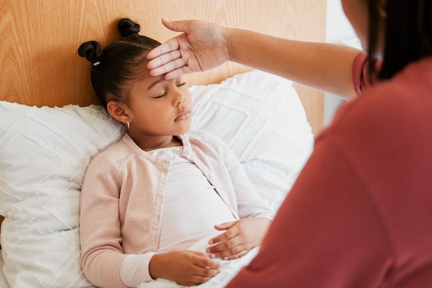 Sick child with mother checking forehead temperature feeling ill and unwell Small girl with illness fever or disease at home in bed resting sleeping and recover from infection flu or covid virus