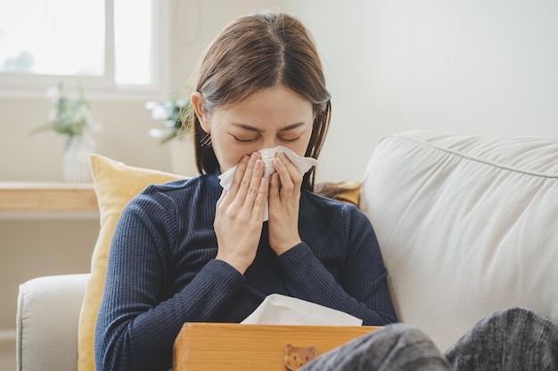 Sick coronavirus covid19 asian young woman girl headache under
blanket have a fever flu and use tissues paper sneezing nose runny
sitting on sofa bed at home health care on virus person